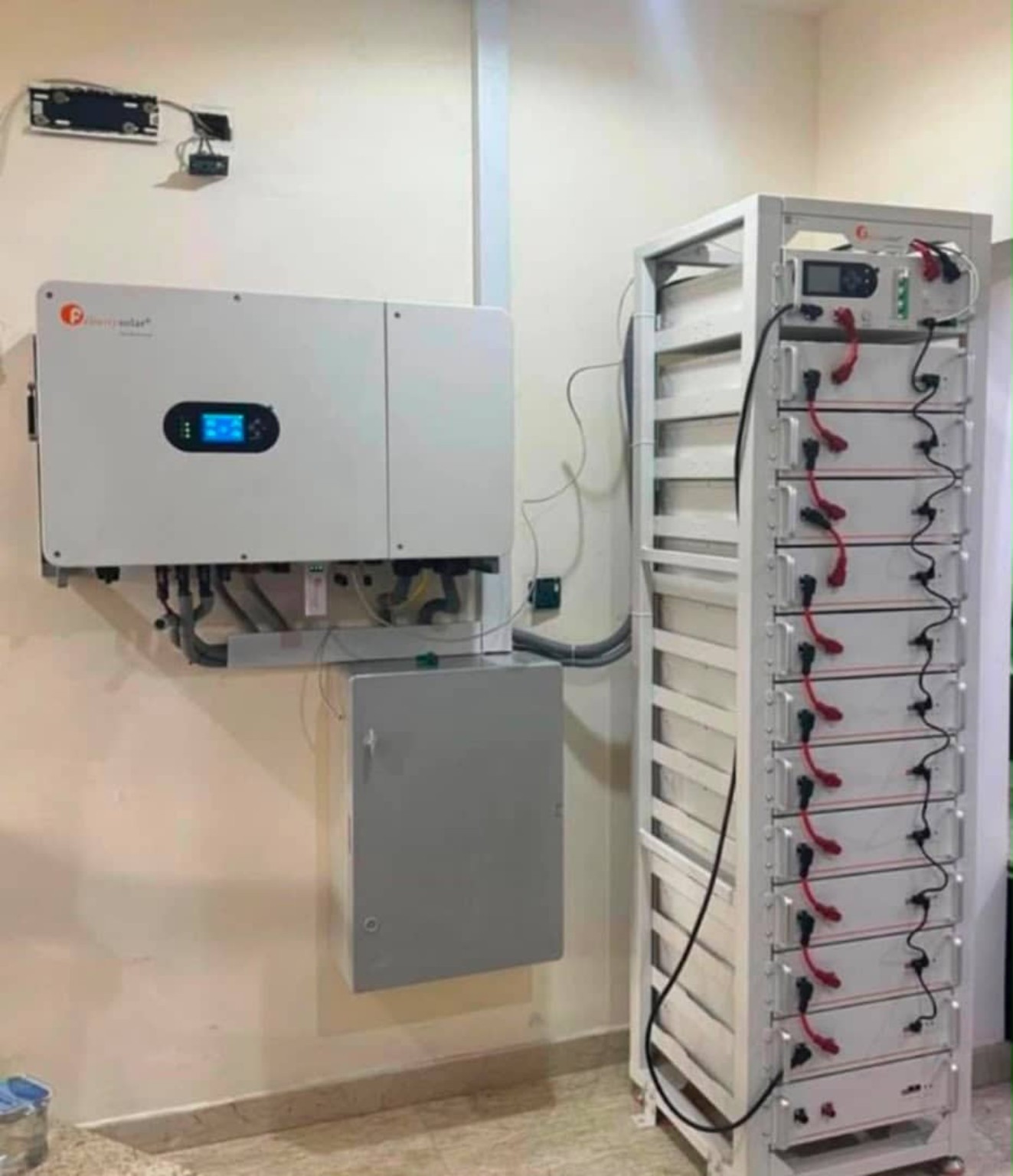 Wall-mounted inverter beside a tall battery rack indoors